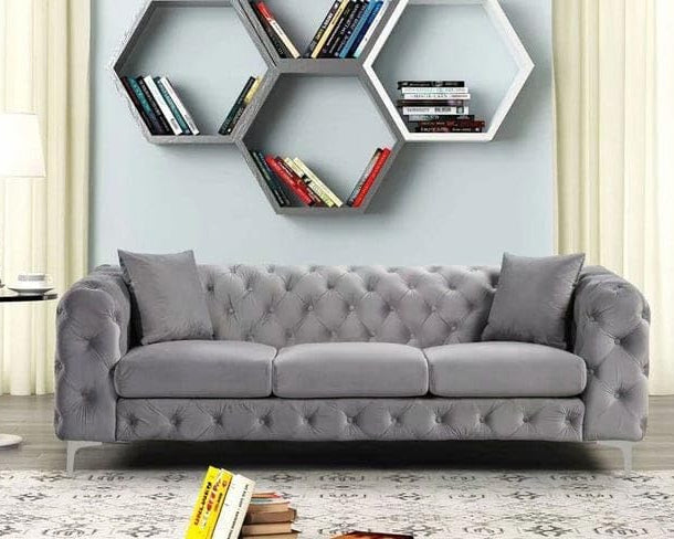Gray tufted sofa in a room with hexagonal bookshelves on the wall.