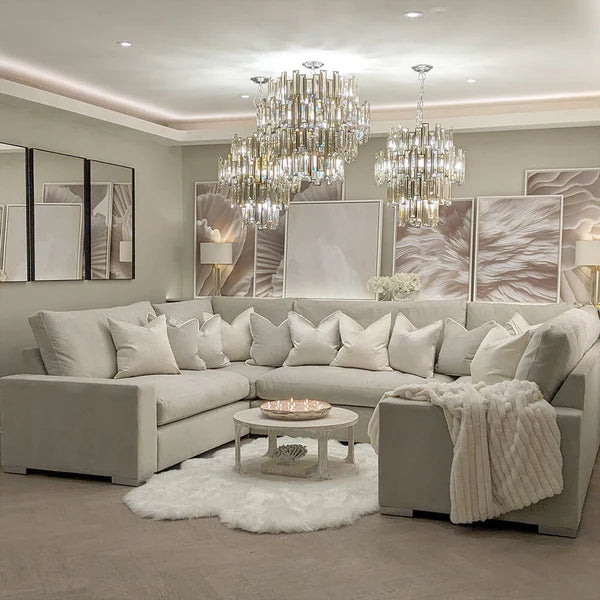 Modern living room with a gray sectional sofa, chandeliers, and decorative elements.