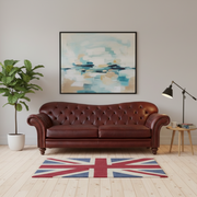 Brown leather sofa in a living room with a Union Jack rug, plant, and abstract painting.