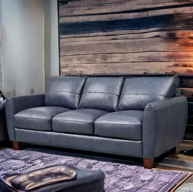 Gray leather sofa in a living room setting with a wooden wall and rug.