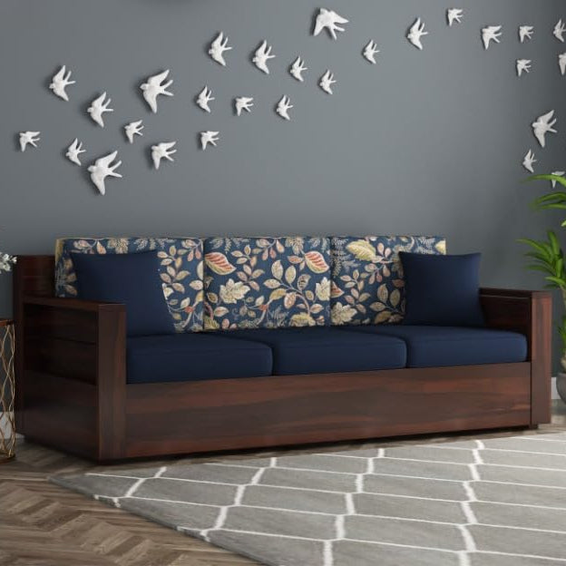 Wooden sofa with floral cushions against a gray wall with decorative white birds.