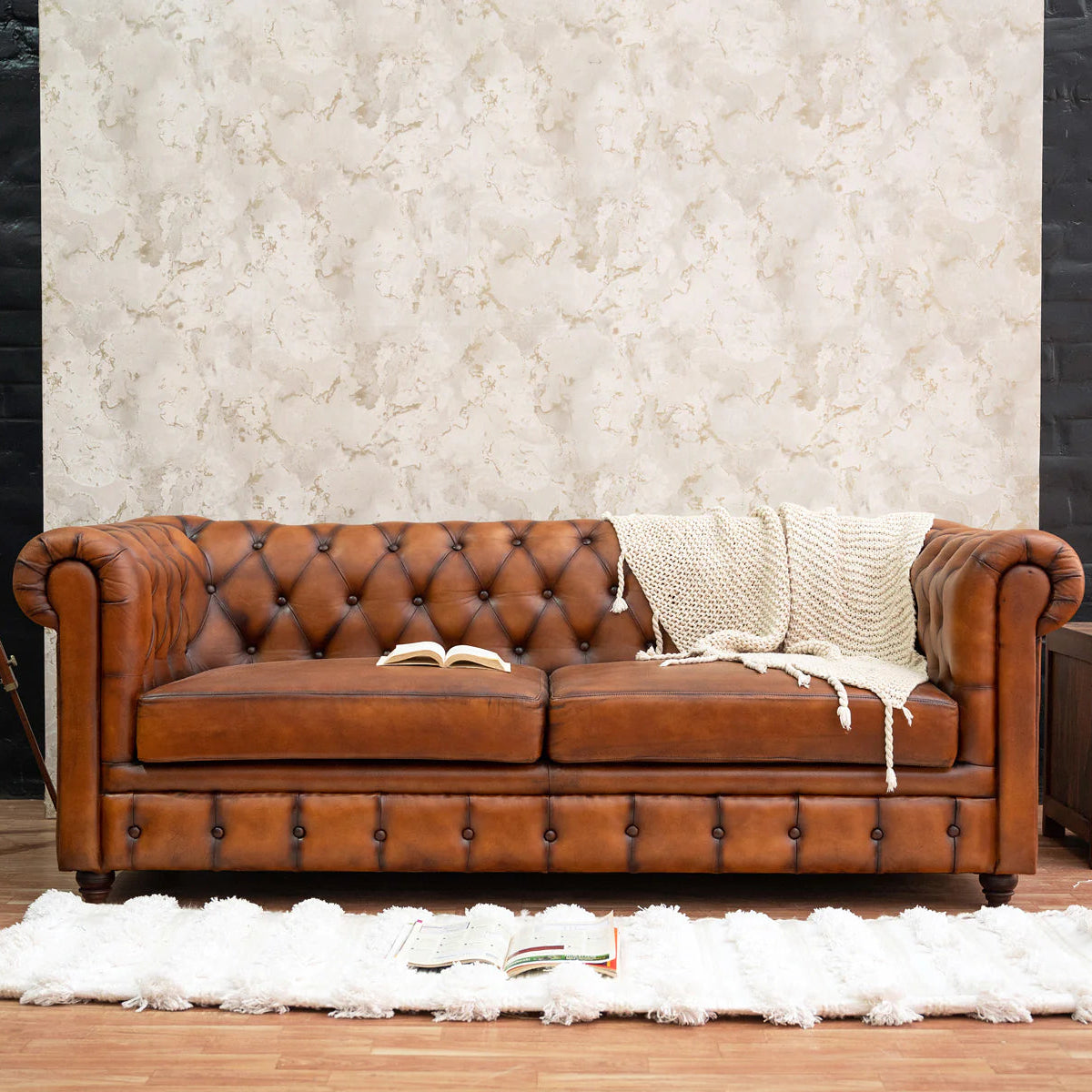 Brown leather sofa with a blanket on a wooden floor against a textured wall.
