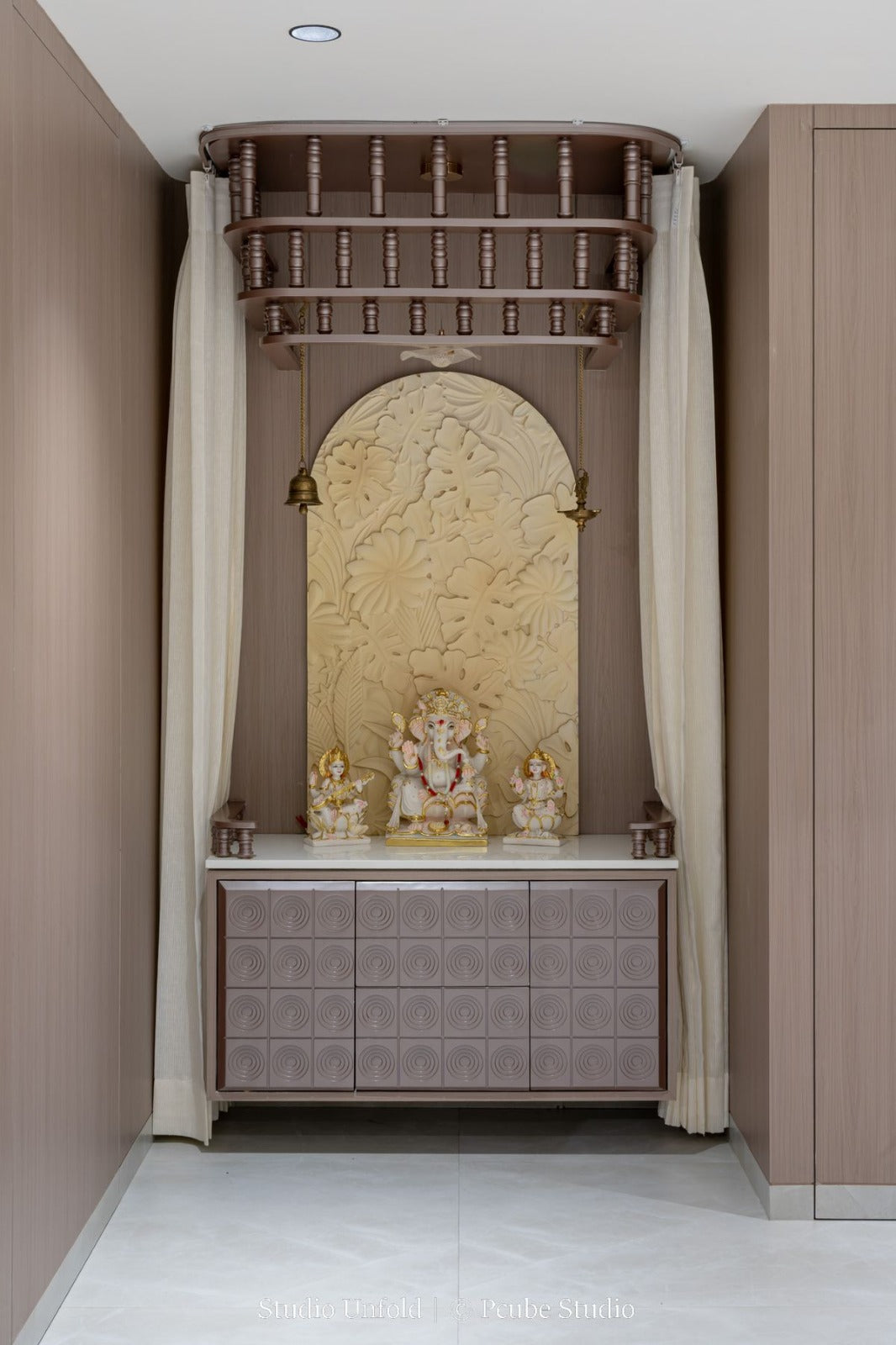 Traditional Pooja Corner with Carved Floral Backdrop & Hanging Bells in Warm Wood Tones